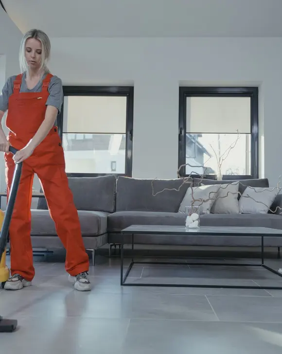 Two cleaners in red overalls working through a living room with a vacuum and a mop