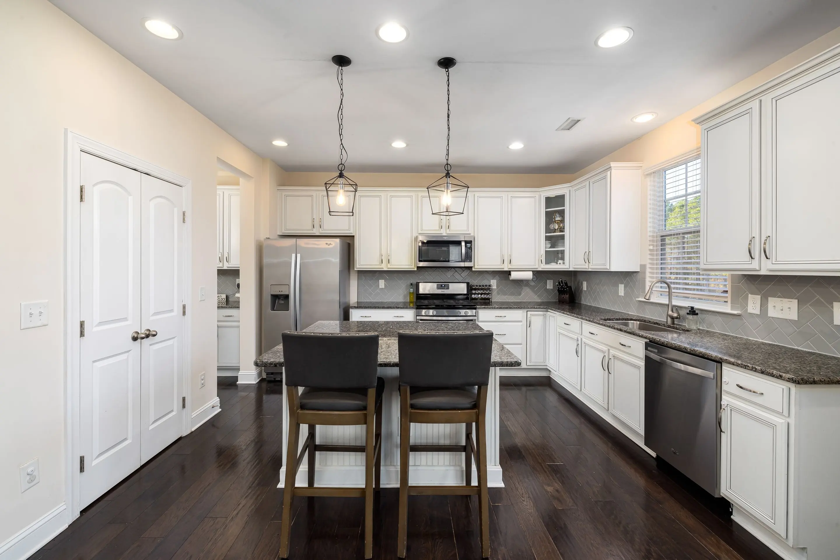 A white kitchen with pendant lights over the island and dark wood floors