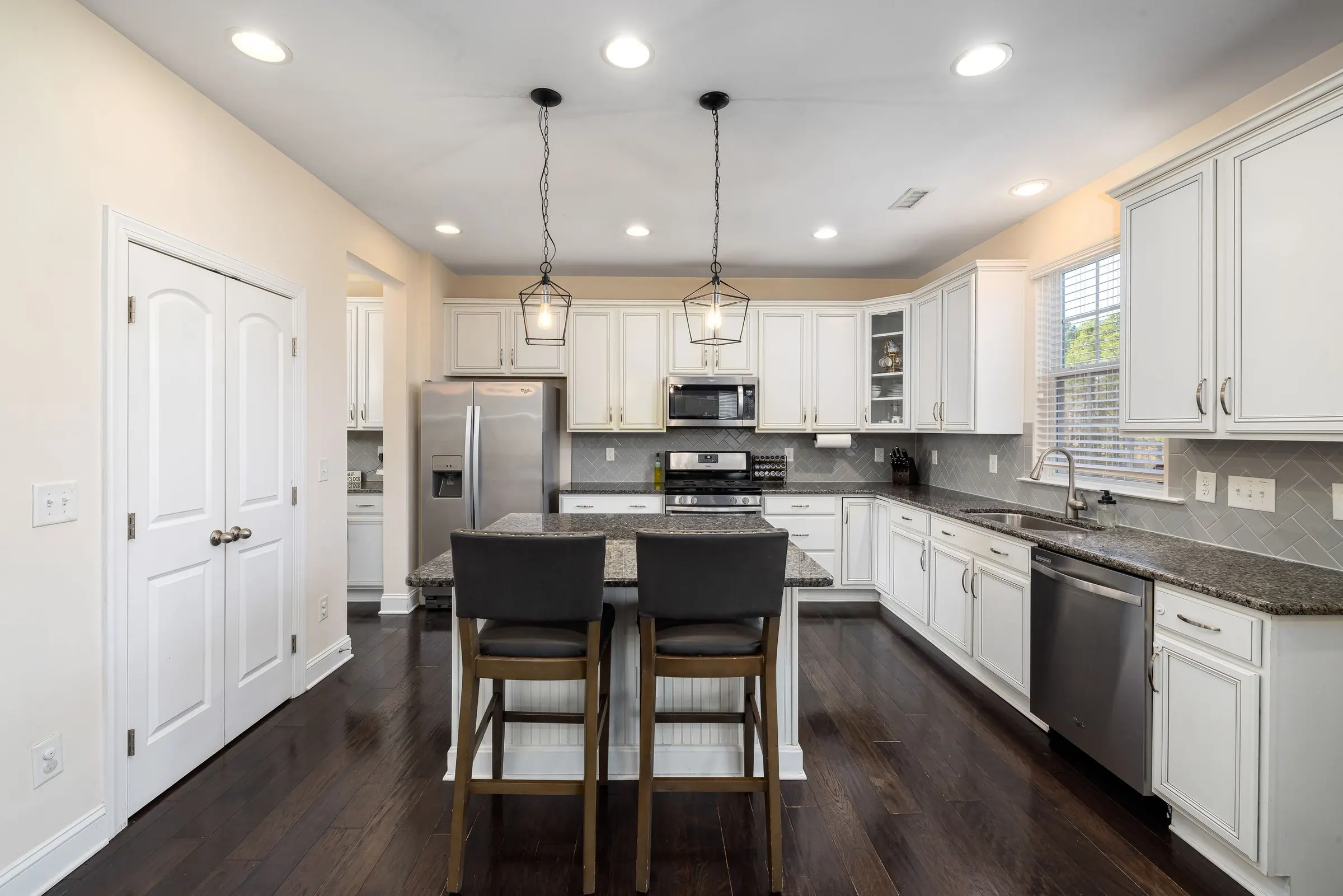 A white kitchen with pendant lights over the island and dark wood floors