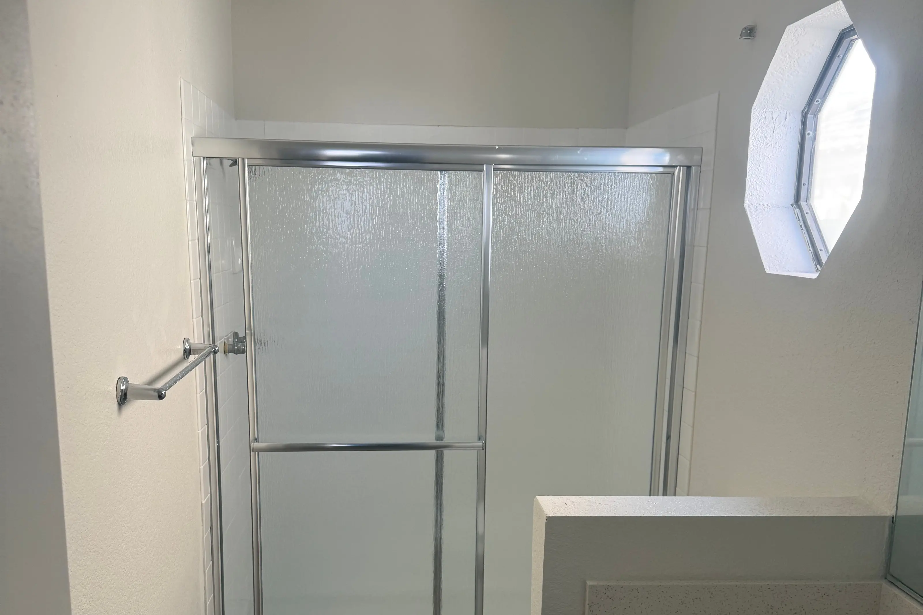 A bathroom with a sliding glass shower door and an octagonal window
