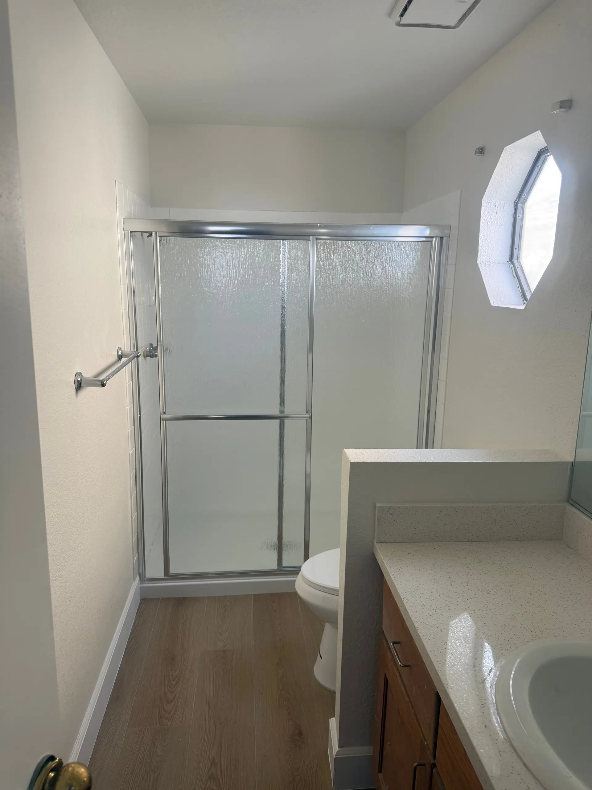 A bathroom with a sliding glass shower door and an octagonal window