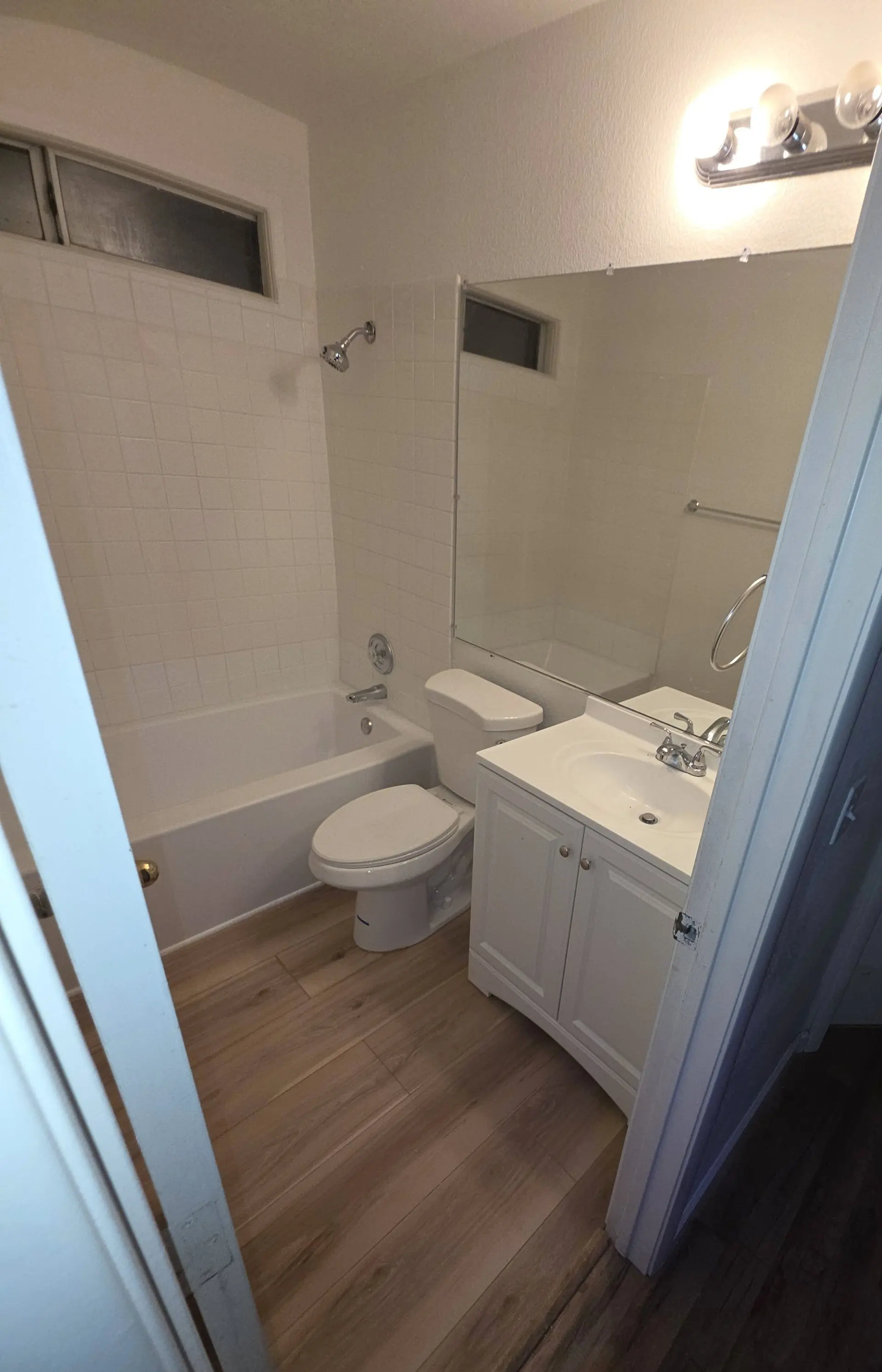 A hall bathroom with a tub, a white vanity and a plank floor