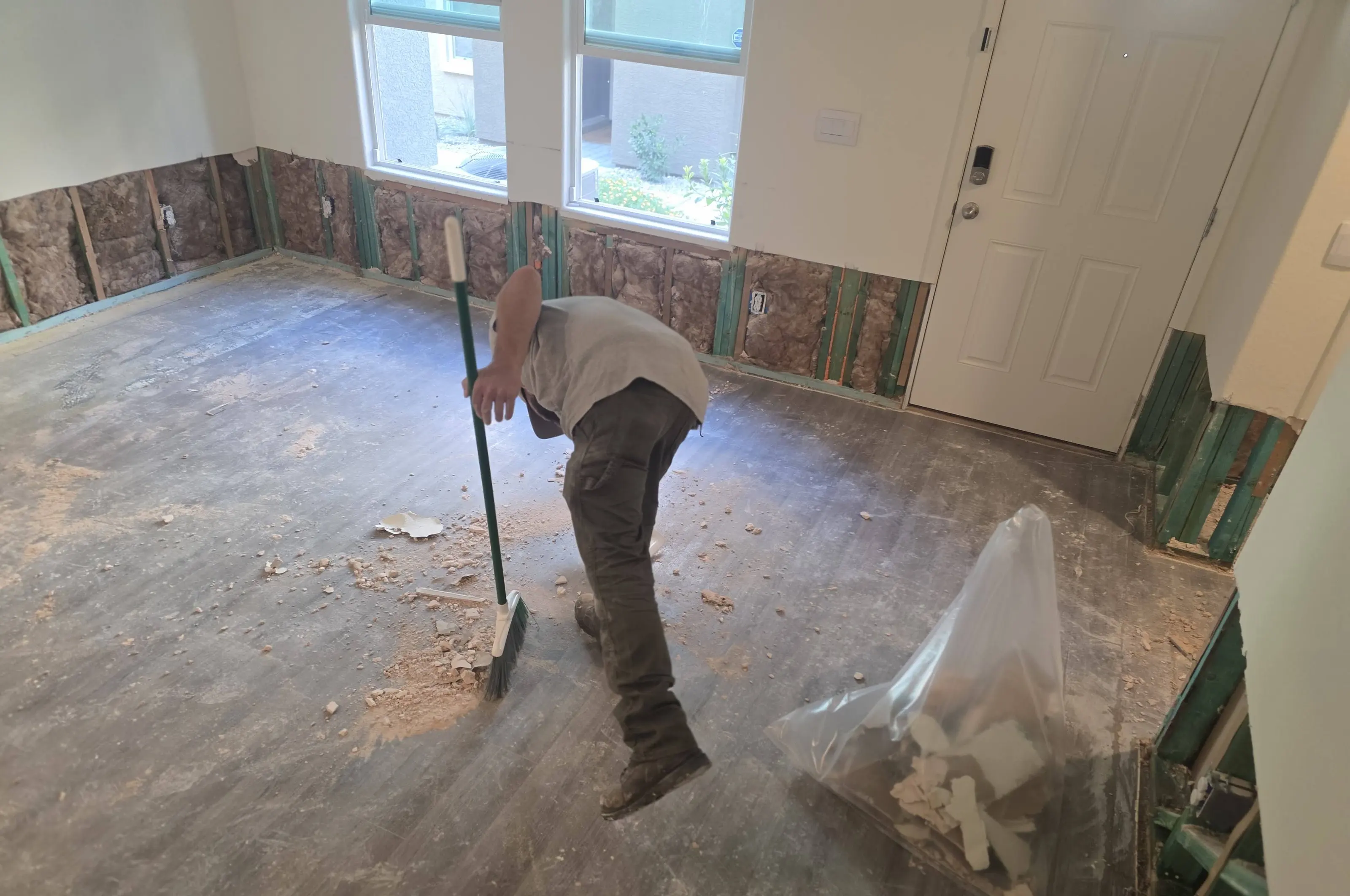 A worker sweeping debris into a bag in a room with the lower wall removed