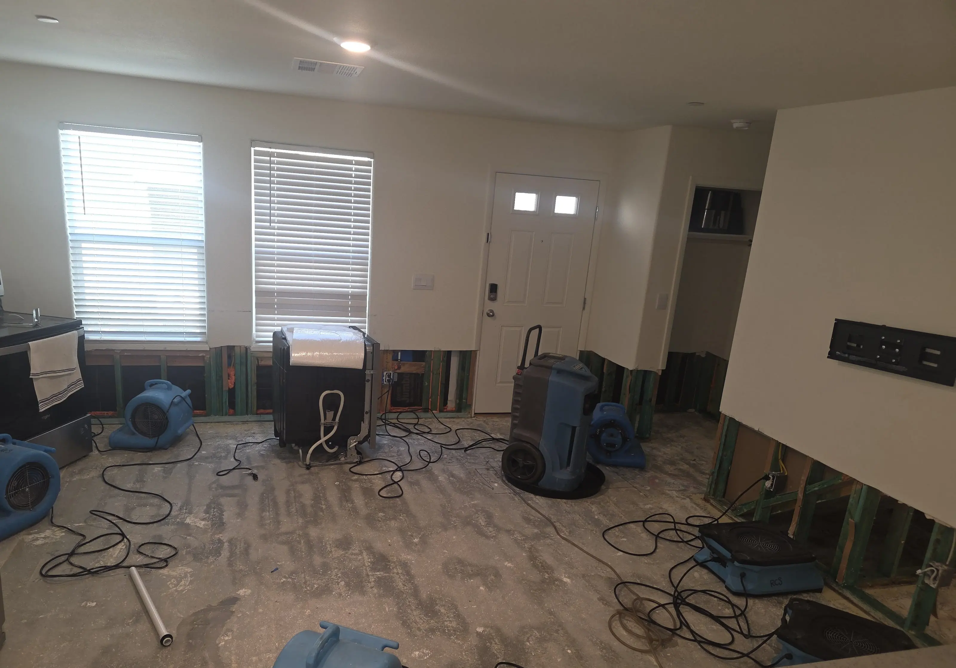 The front of a room with air movers and a dehumidifier on a bare floor
