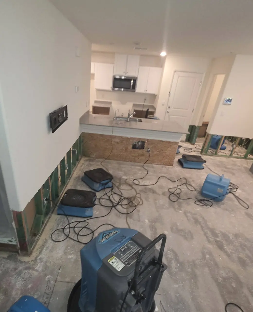 An open-plan room with plastic containment and air movers drying the floor