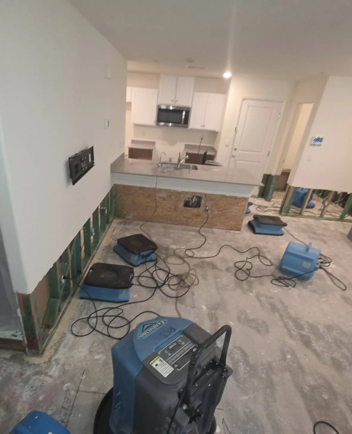 An open-plan room with plastic containment and air movers drying the floor