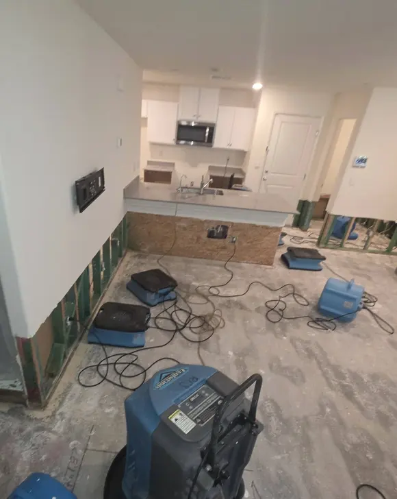 An open-plan room with plastic containment and air movers drying the floor