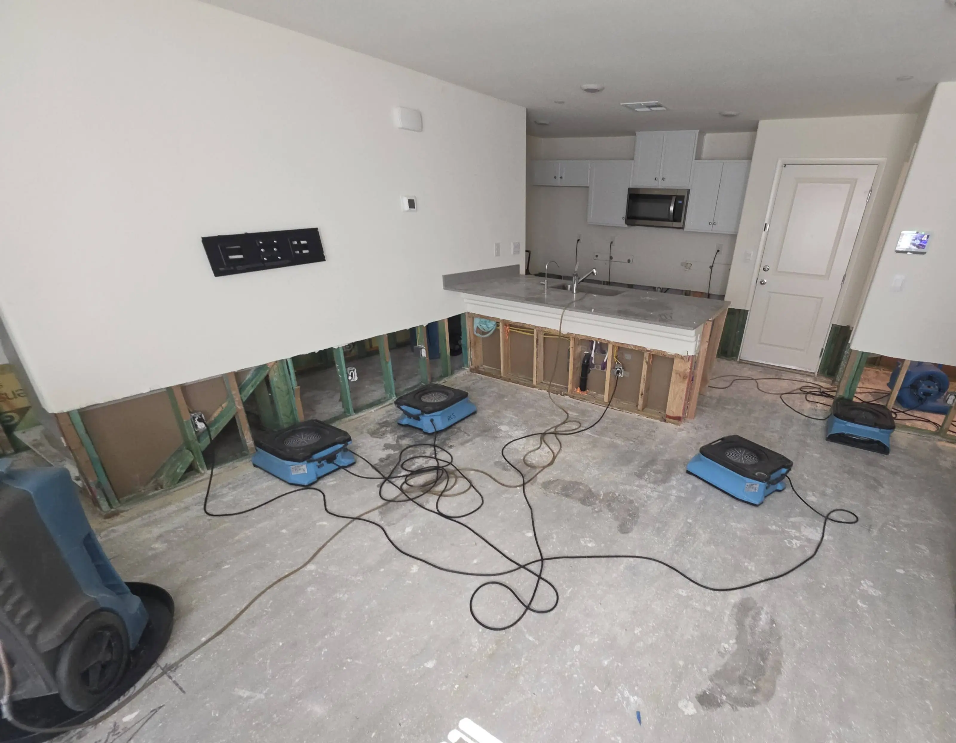 A kitchen and living area with the lower wall cut out and air movers on a bare slab