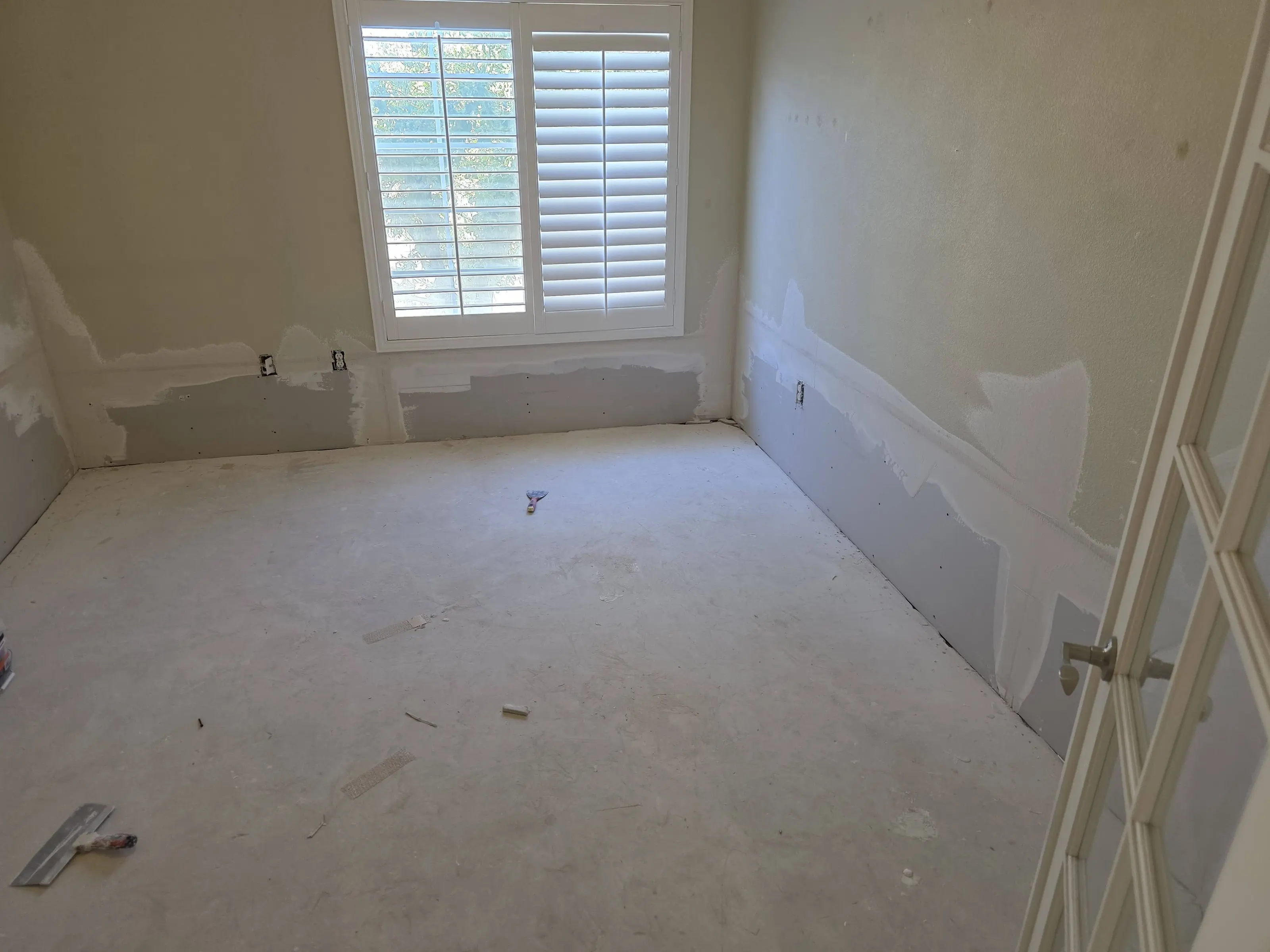 A bedroom with new drywall patched in along the bottom of the walls and the first coat of joint compound on, over a bare slab