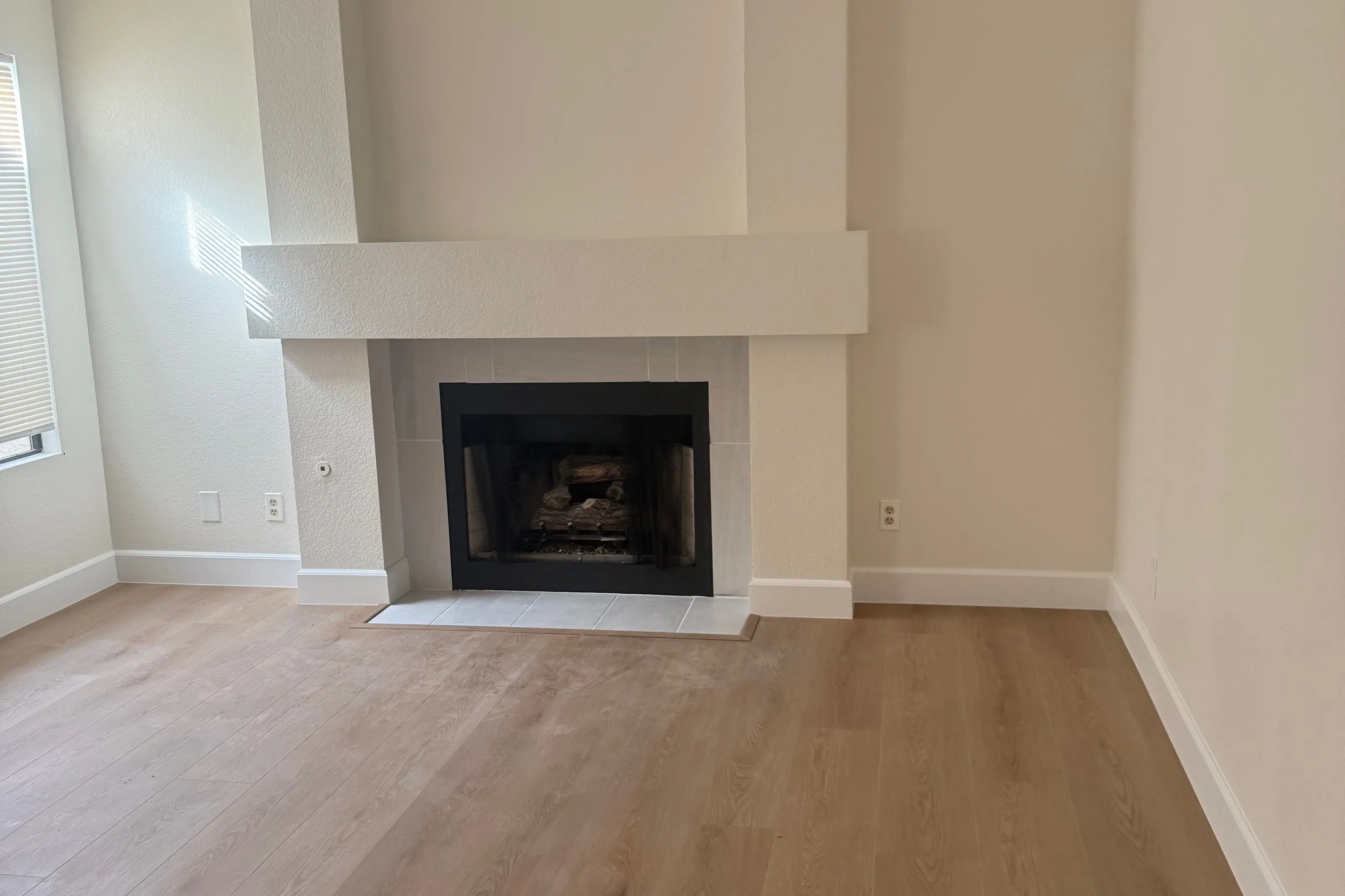 A living room with a white fireplace and a light plank floor