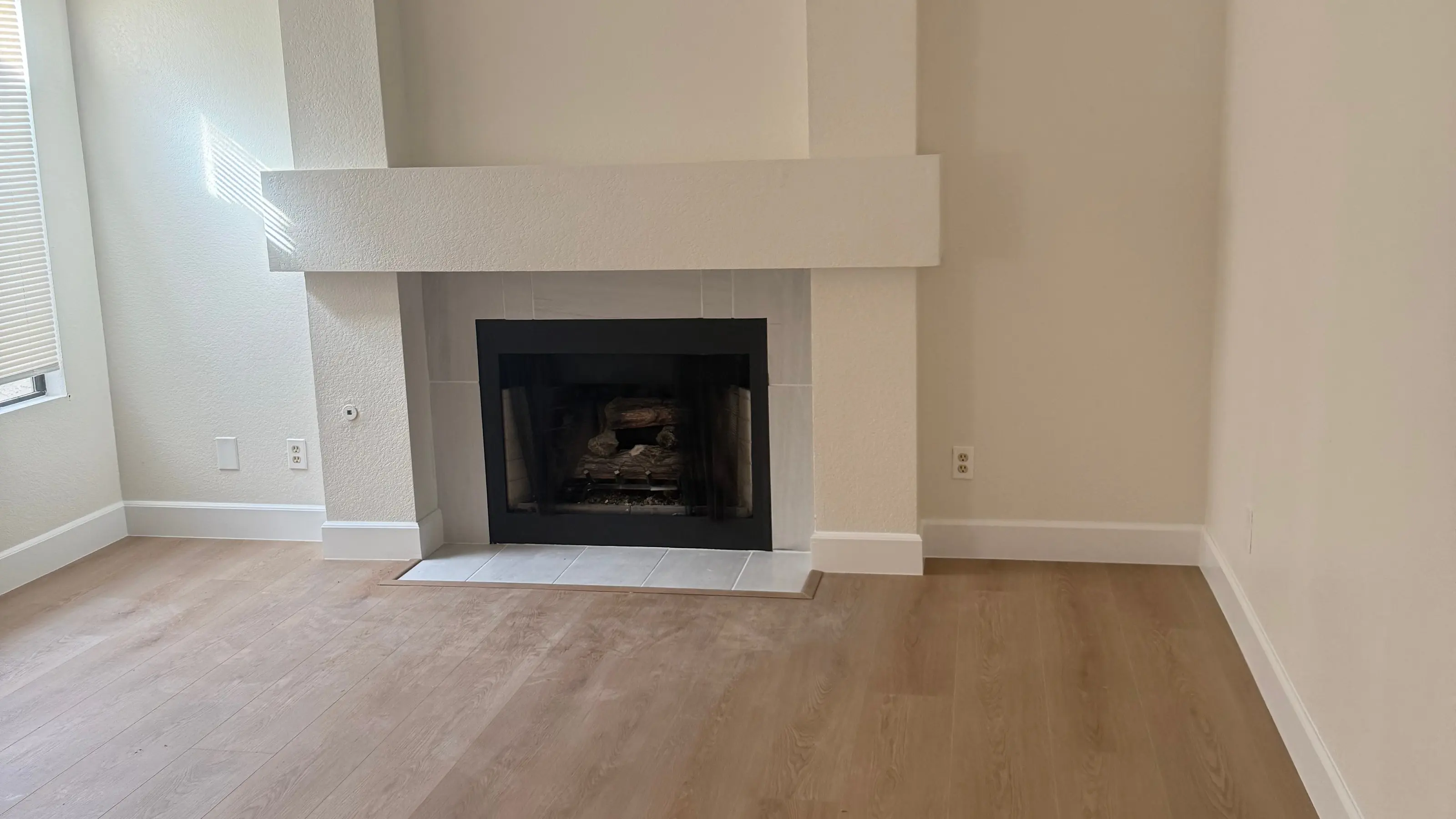 A living room with a white fireplace and a light plank floor