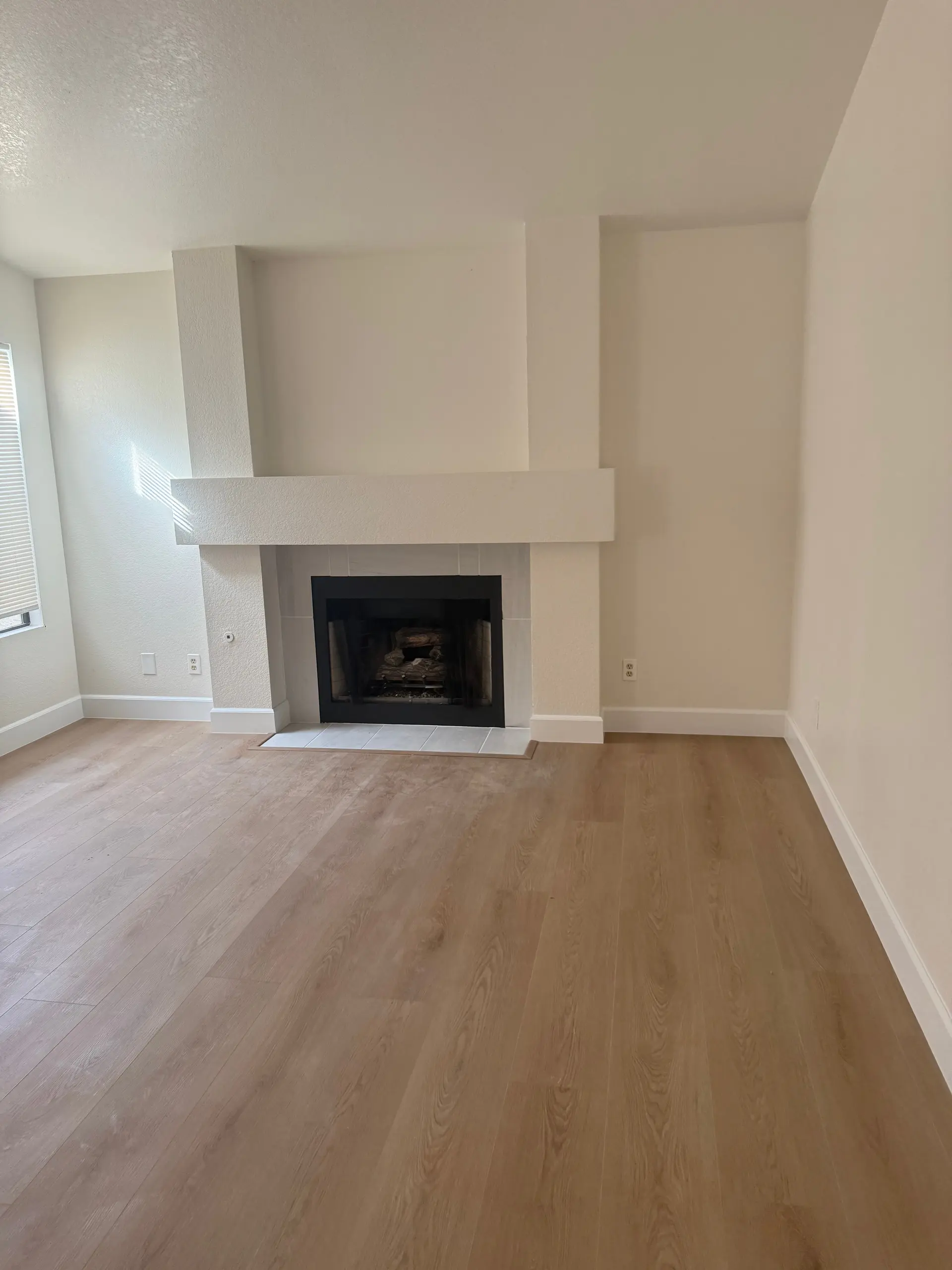 A living room with a white fireplace and a light plank floor