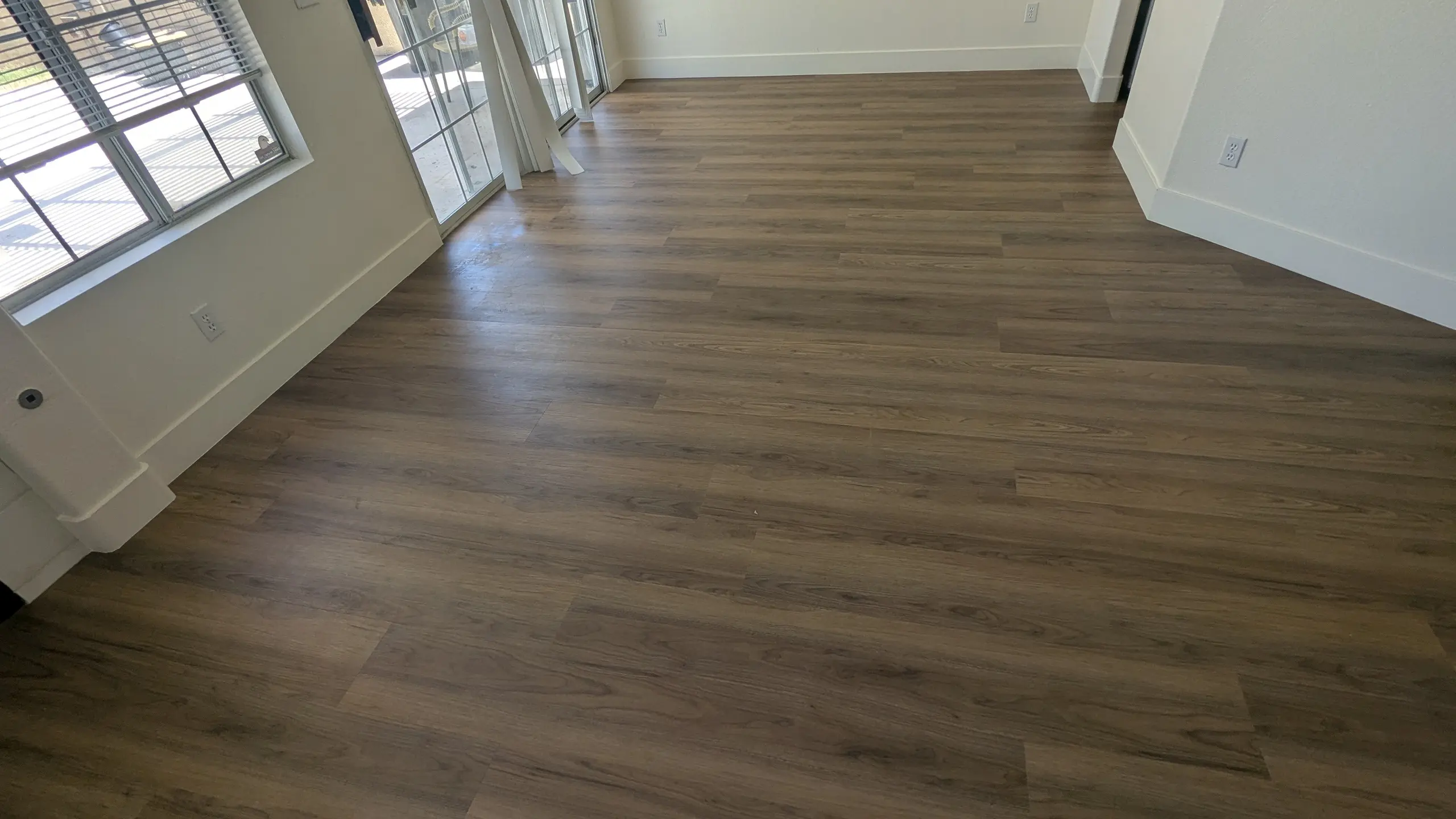 A long run of dark plank flooring reaching the patio doors