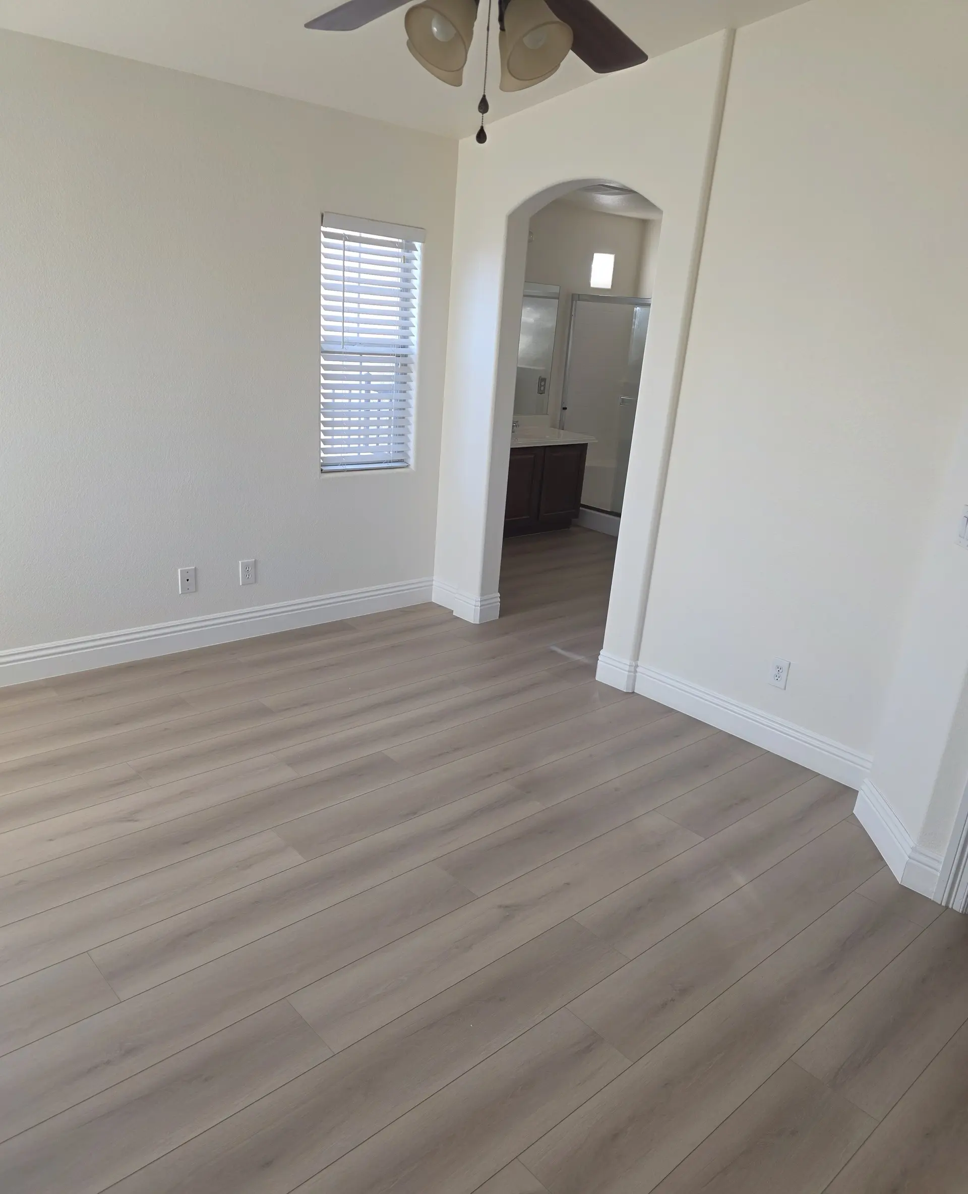 A bedroom with light plank flooring and an arched opening