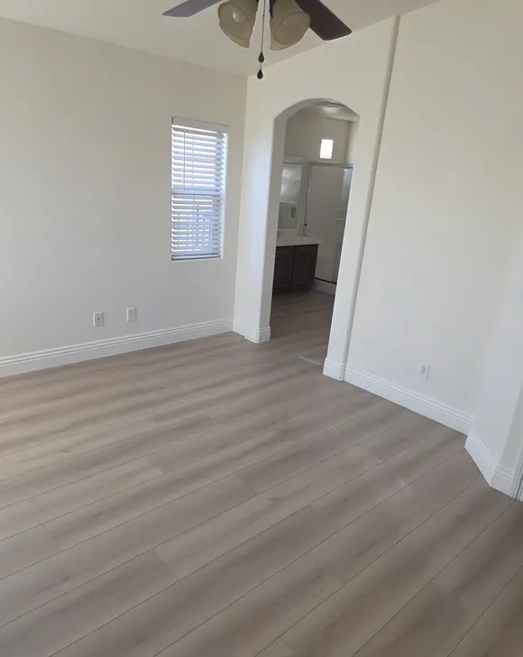A bedroom with light plank flooring and an arched opening