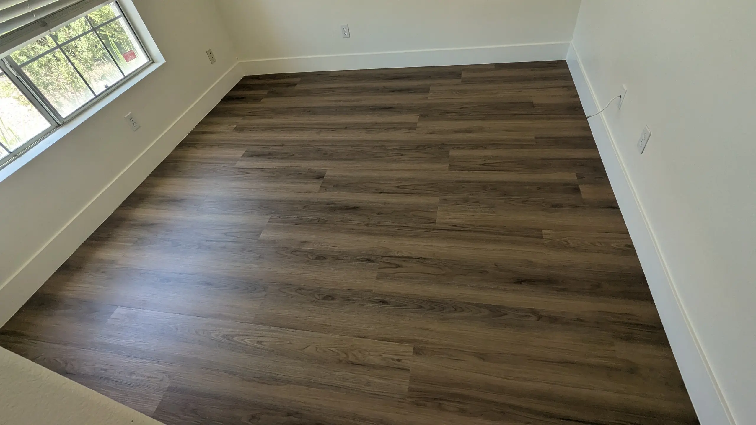 A room with dark plank flooring and a window