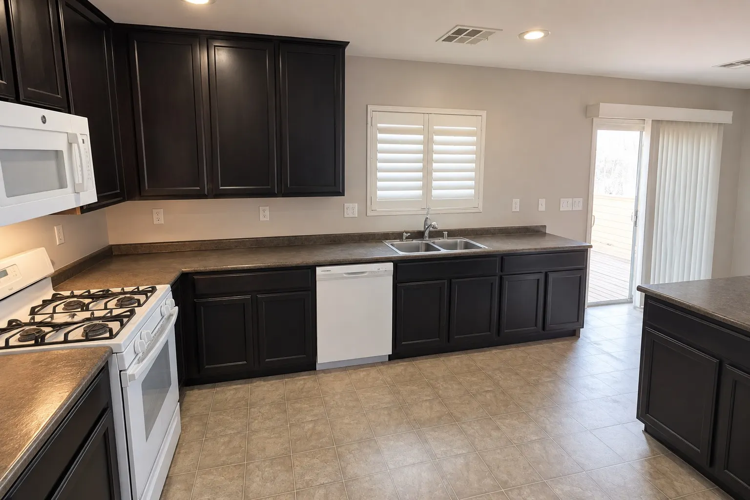 A kitchen with dark cabinets, speckled brown counters, white appliances, a shuttered window and a sliding glass door