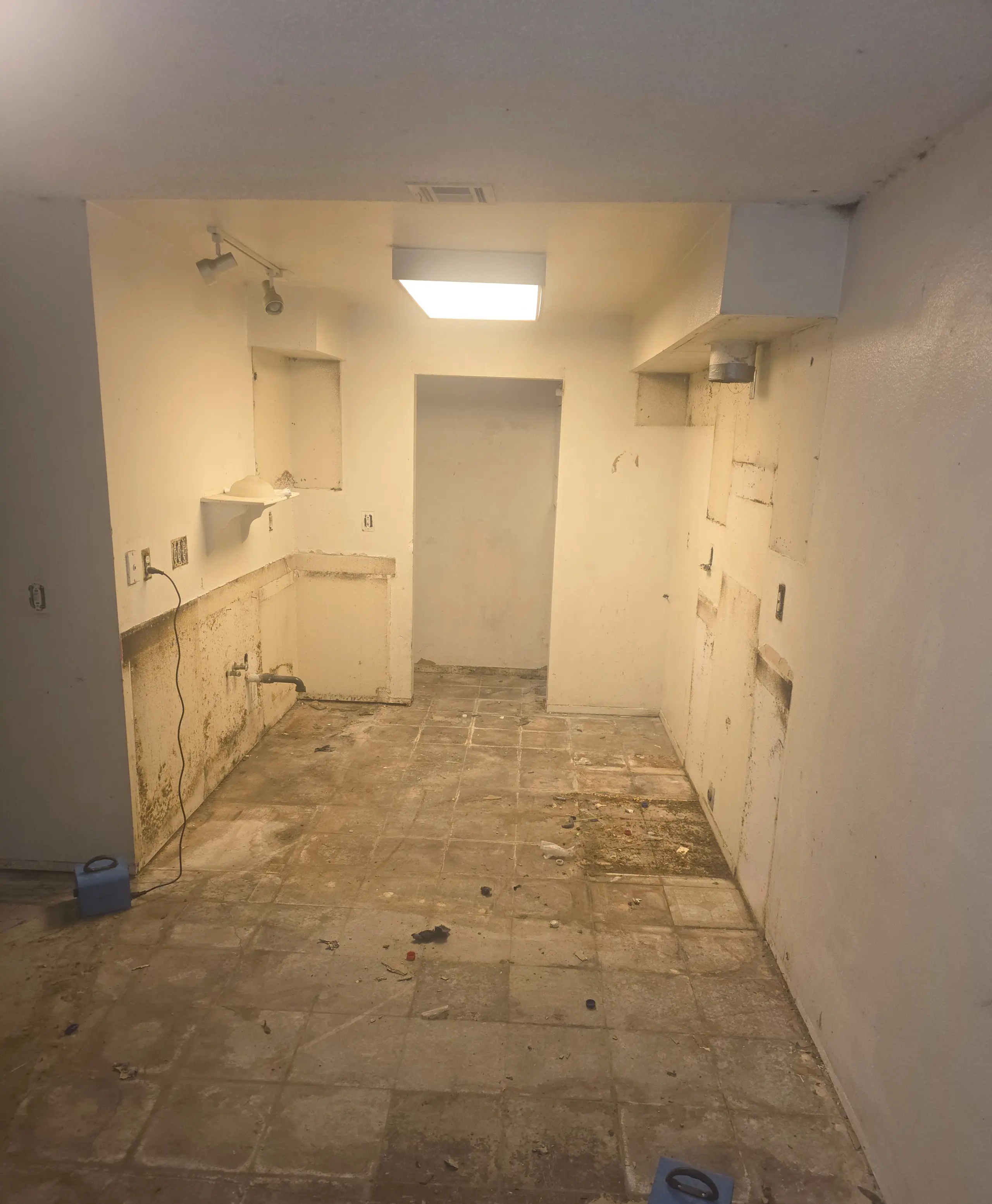 A galley kitchen stripped back, with a stained and worn floor, before the rebuild