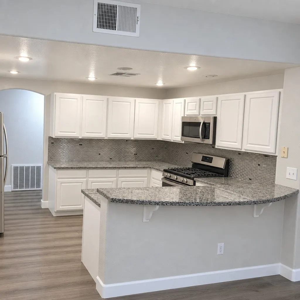 A white kitchen with a curved grey granite peninsula, a silver mosaic backsplash and stainless appliances