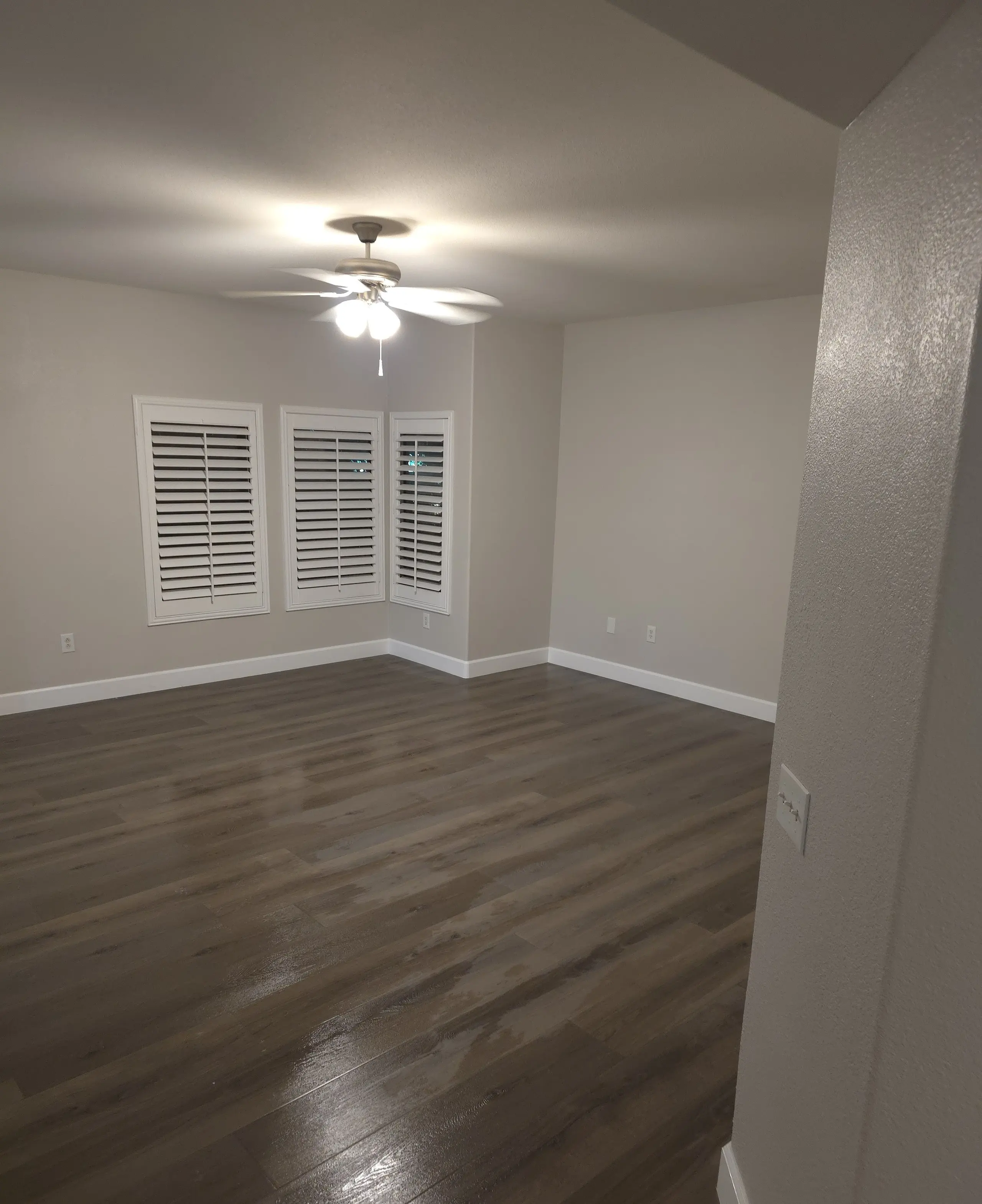 A living room corner with shuttered windows, fresh paint, new baseboards and a dark plank floor