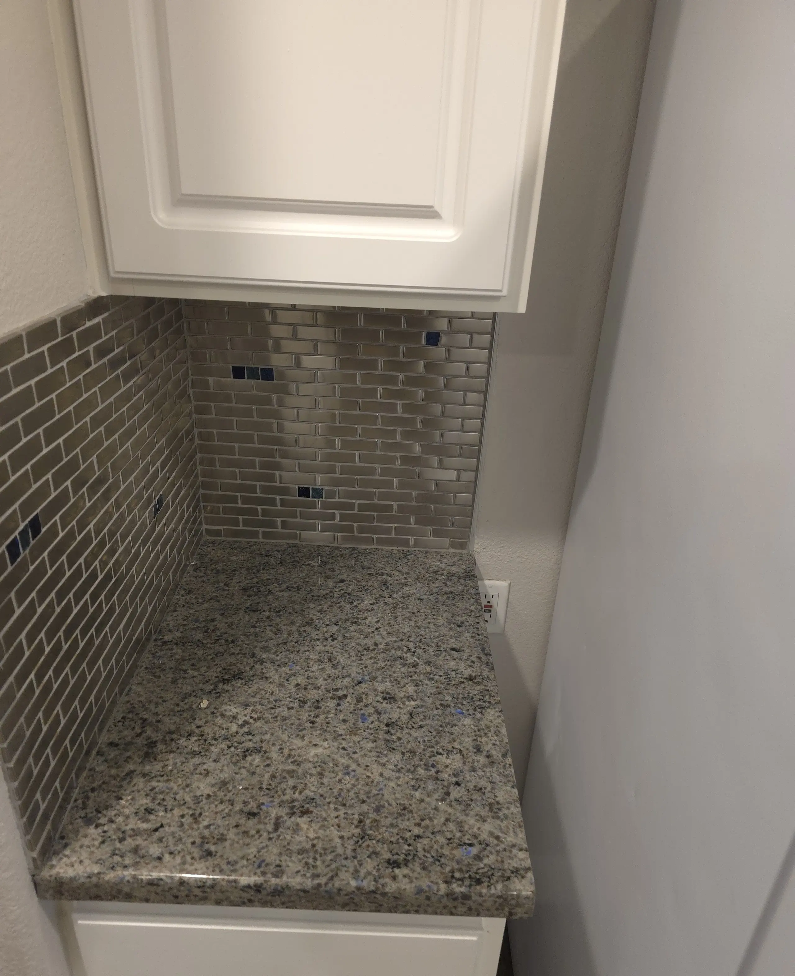 A clean kitchen corner with a white cabinet, a tiled backsplash and a granite counter
