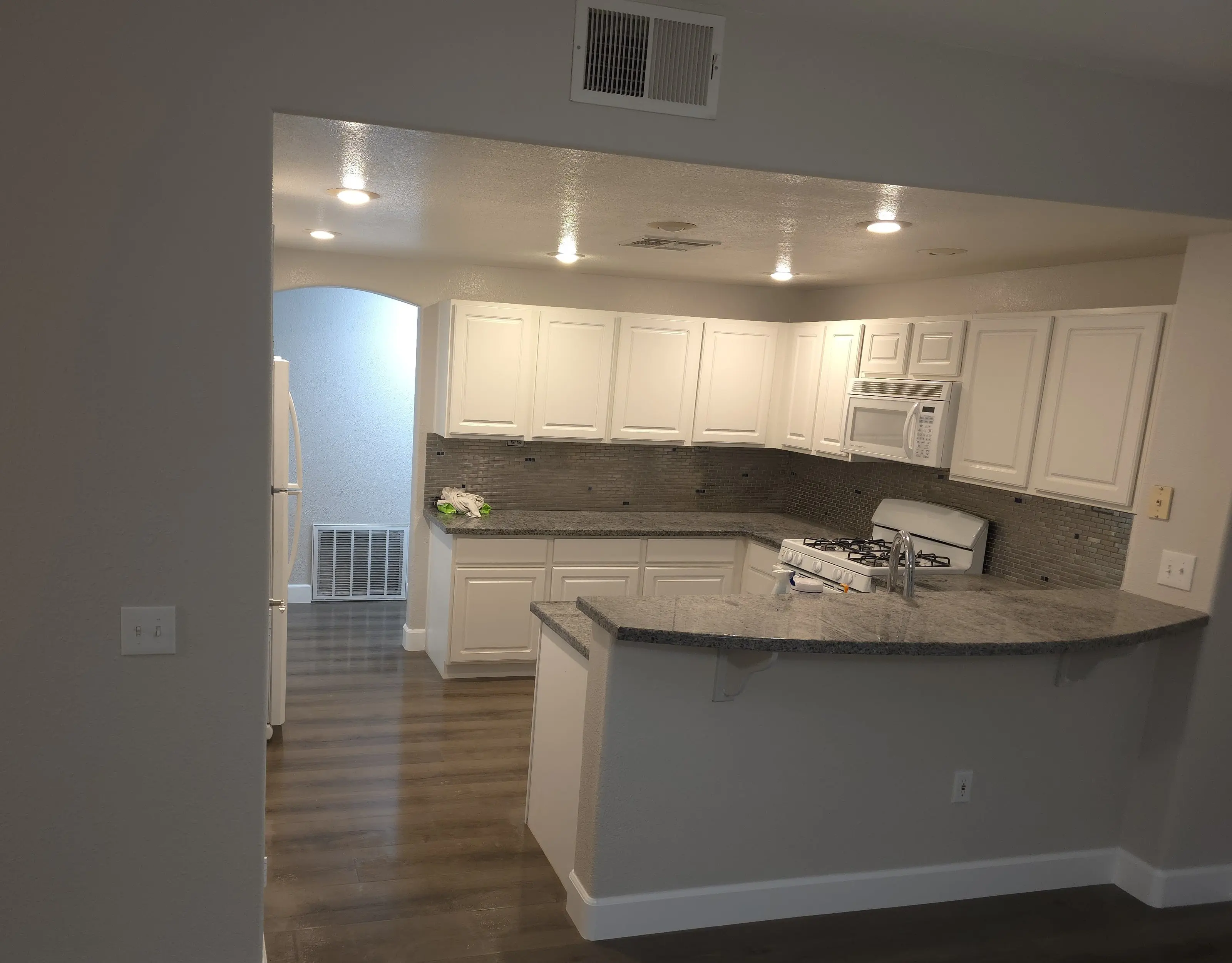 A kitchen and living area after a water damage rebuild, with fresh paint, new baseboards and a dark plank floor