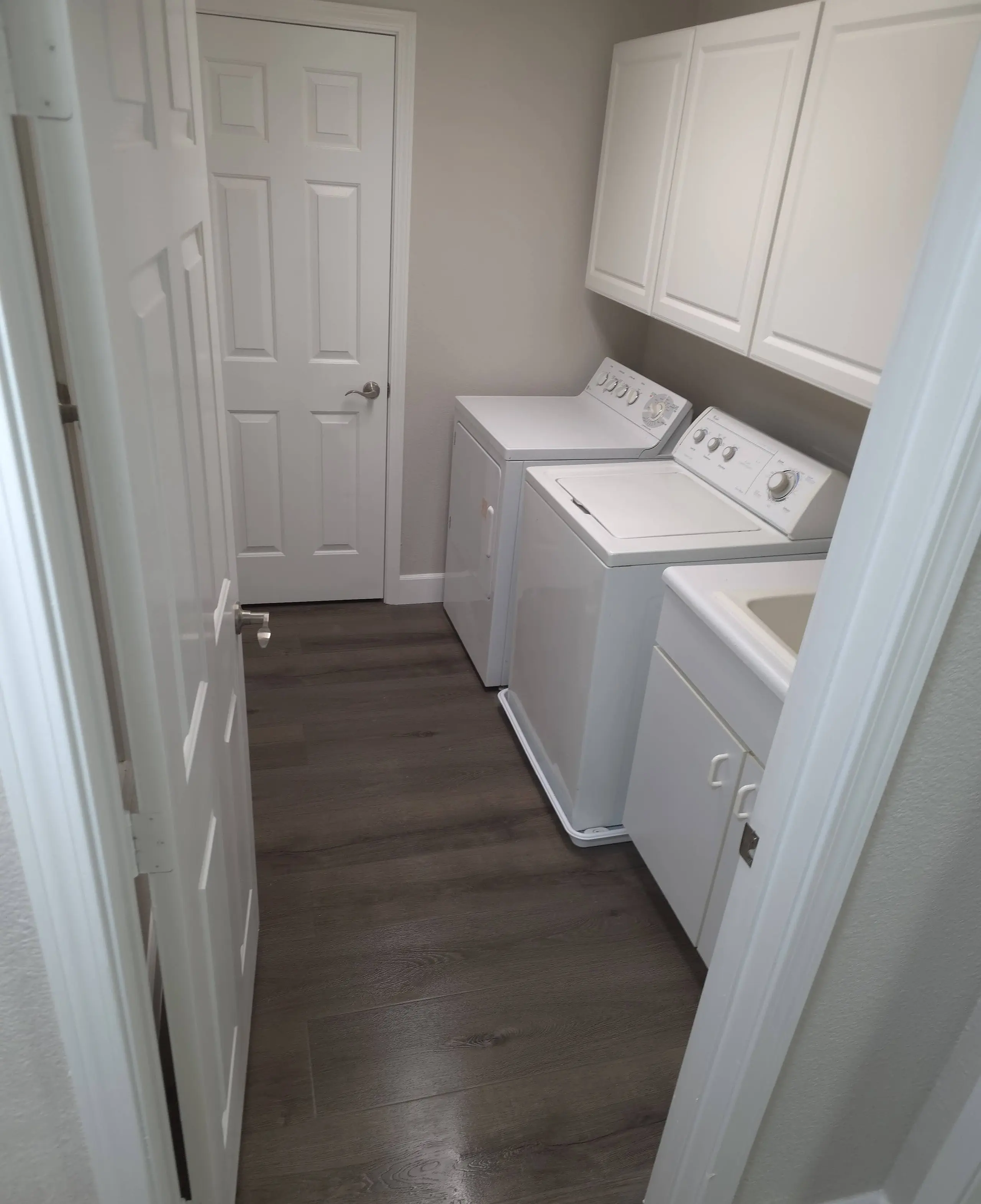 A laundry room with a washer, a dryer, a utility sink and a new plank floor