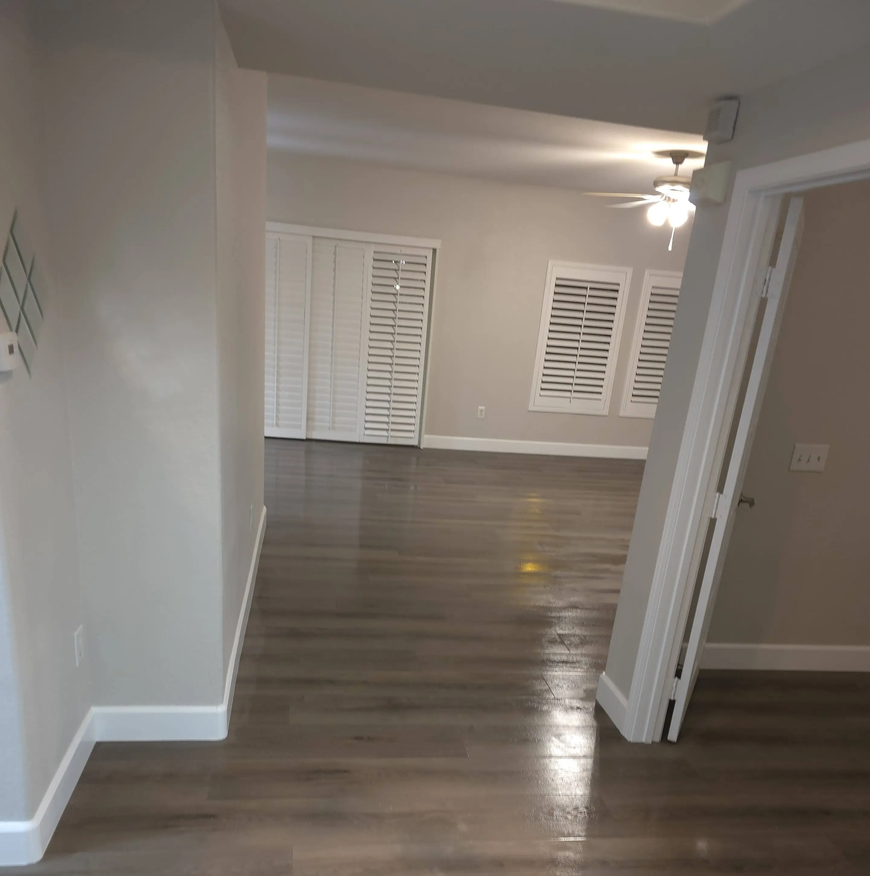 A hallway opening into a living room with shuttered windows, fresh paint and a new plank floor