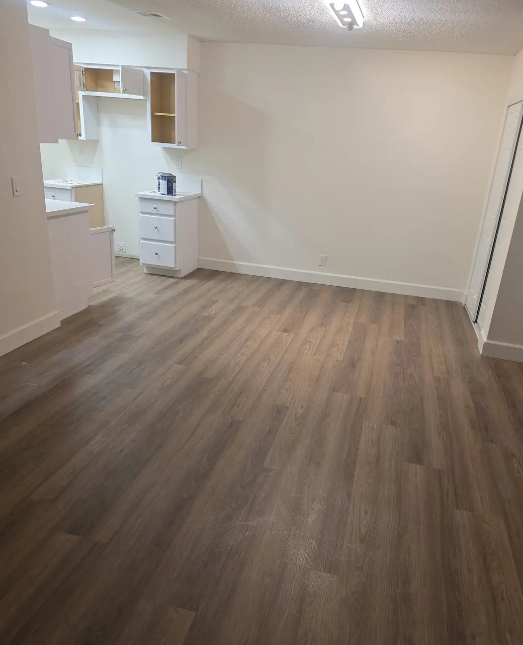 A long room with freshly painted walls and a new plank floor, with kitchen cabinets still being fitted at the far end