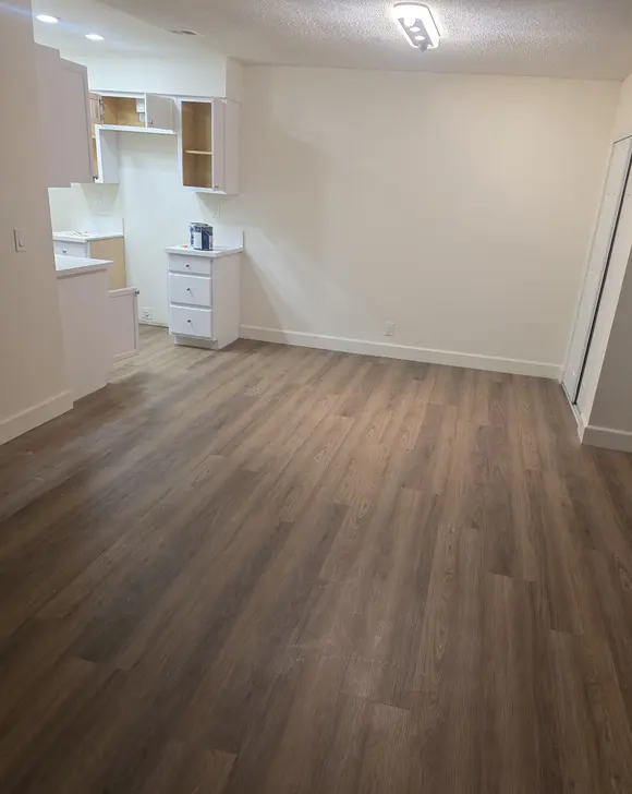 A long room with freshly painted walls and a new plank floor, with kitchen cabinets still being fitted at the far end