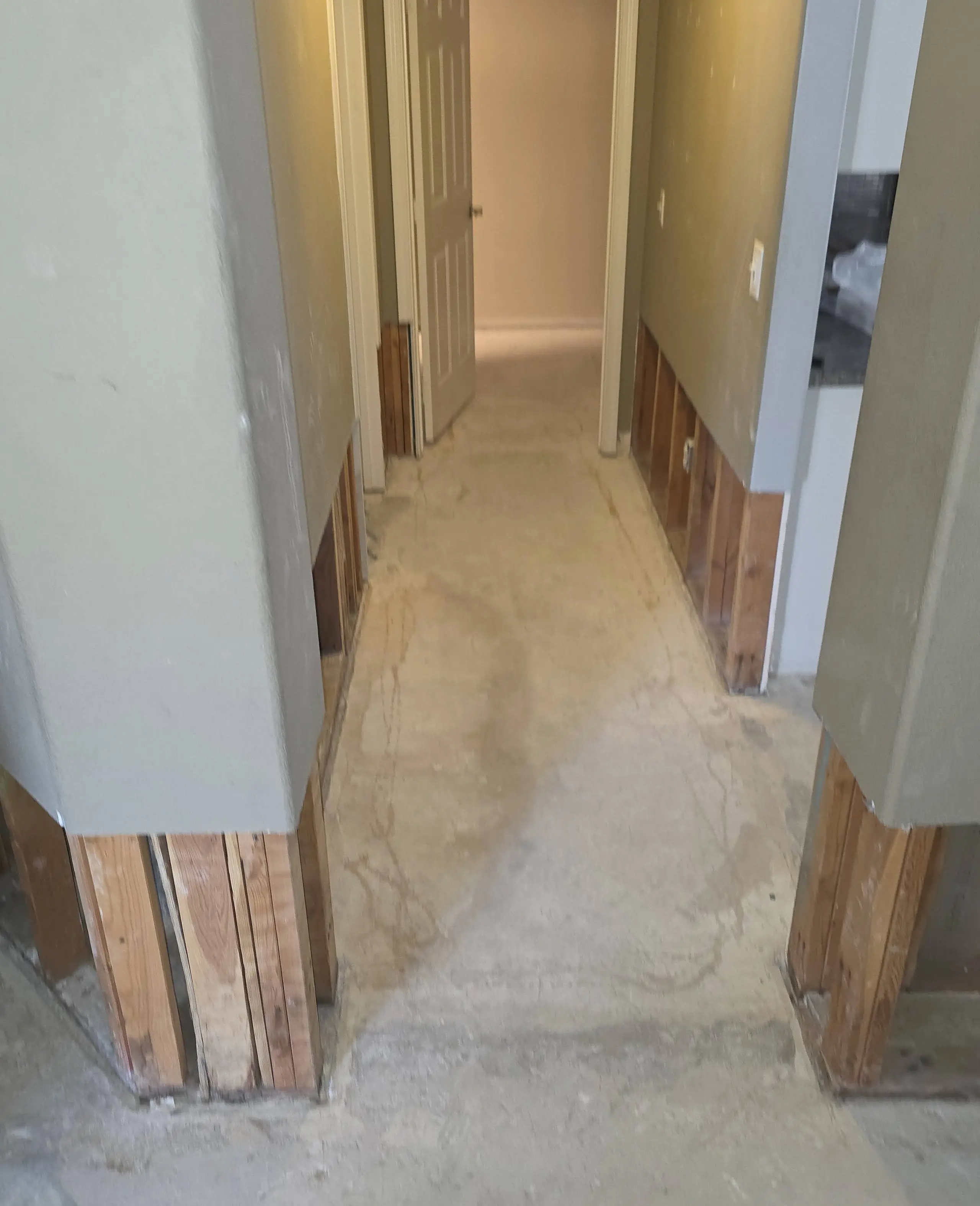 A hallway with the lower walls cut away to the studs and the floor taken up to the bare slab, after a water loss