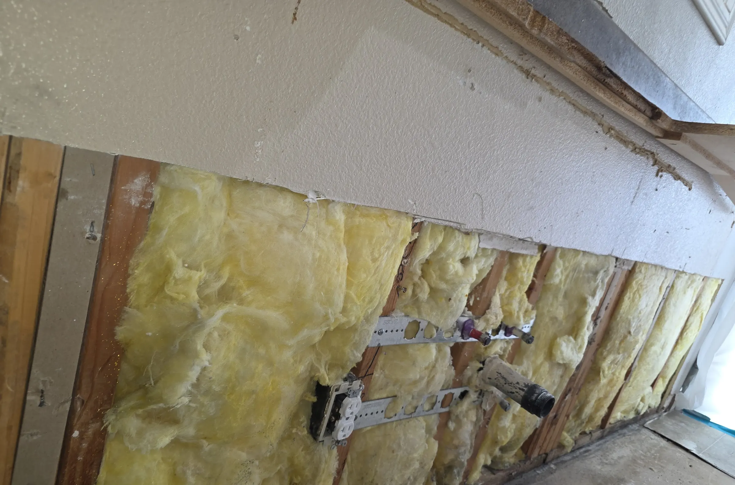 A wall opened back to yellow insulation and framing after mold removal